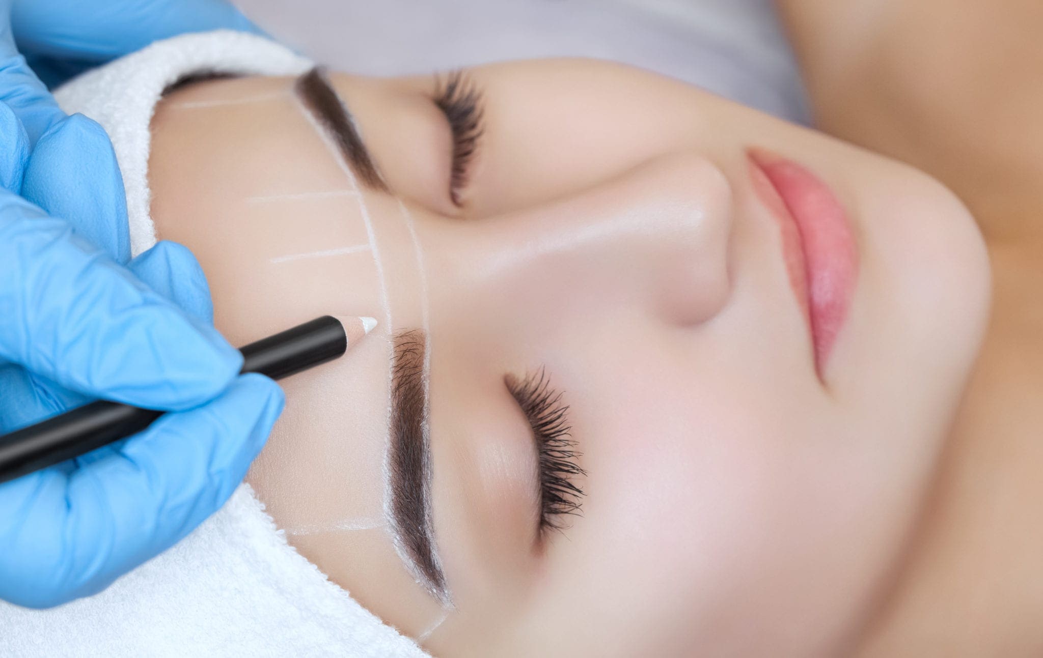 Permanent make-up for eyebrows of beautiful woman with thick brows in beauty salon. Closeup beautician doing tattooing eyebrow. Nanoblading alternate to Microblading